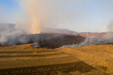 Aerial view of spring dry grass burning field. Fire and smoke in the meadow, nature pollution and danger,common waste are burned