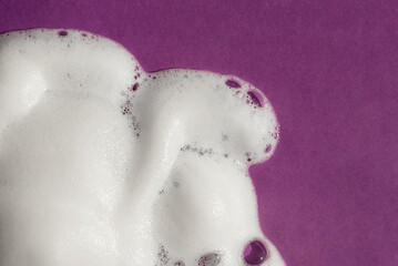 Foam on a purple background. Soapy liquid texture with bubbles. Natural sunshine and shadows. Skin care cleansing cosmetic in top view.