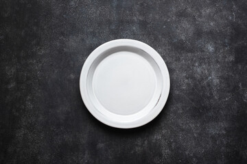 Empty ceramic plate on black concrete background texture. Top view, copy space for text or design