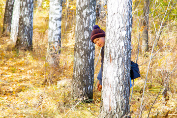 cheerful boy hiding behind a tree on an autumn day