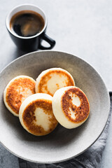 Cottage cheese fritters in craft ceramic bowl served with cup of espresso coffee, closeup view. Breakfast food