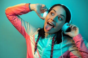 Happy young woman in 90s style sport outfit with white headphones dance in neon lights at studio.