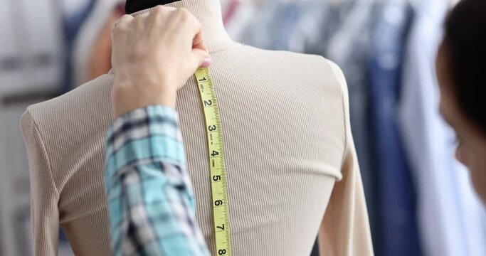Seamstress takes measurements from mannequin in atelier
