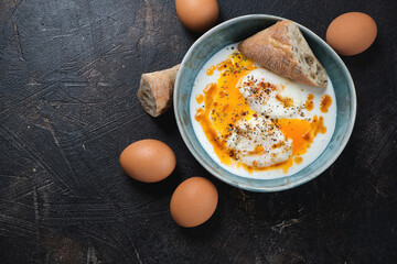 Cilbir or a turkish dish of poached eggs with yogurt, flat lay on a dark-brown stone background, horizontal shot with space