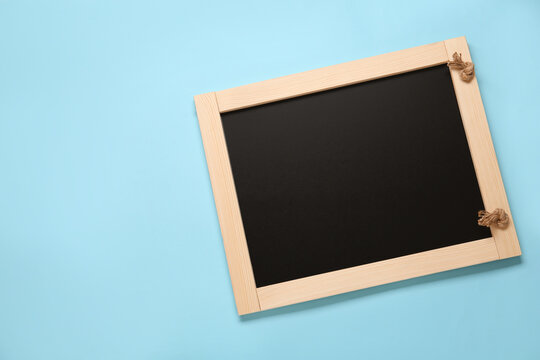 Clean small black chalkboard on light blue background, top view. Space for text