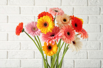 Bouquet of beautiful colorful gerbera flowers in vase against white brick wall