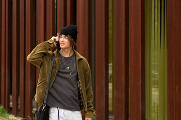 young man talking on mobile phone walking down the street in autumn