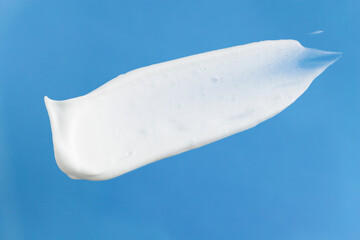 Smear of white cream on a blue background, top view. Cosmetic product for skin care, body lotion, shampoo, foam close-up.