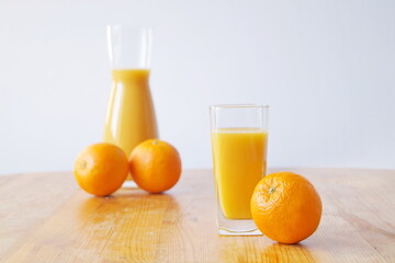 Fototapeta na wymiar There is a glass with freshly prepared orange juice on a wooden table, a jug of juice is standing next to it, oranges are also on the table - a charge of vitamin C and cheerfulness for the whole day