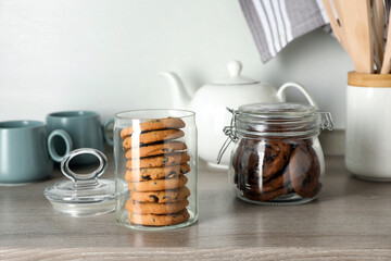 Delicious chocolate chip cookies in glass jars on wooden table in kitchen
