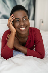 Portrait Black African woman laying on bed, smiling, hand on face