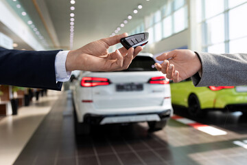 an employee of a car store handing over the keys to a new car to a buyer close-up against the...