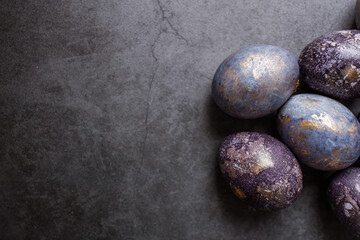 Fototapeta na wymiar Purple, blue and golden eggs on a dark concrete background. The purple hue trend of 2022 is very peri. Easter card with a copy of the place for the text. Natural dye karkade tea. Top view.