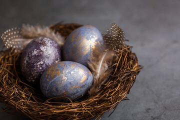 Purple, blue and golden eggs with lavender on a dark background. The purple hue trend of 2022 is very relevant. Natural dye karkade tea. Top view. Easter card with a copy of the place for the text. 