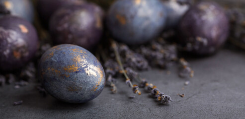 Purple, blue and golden eggs with lavender on a dark background. The purple hue trend of 2022 is very relevant. Natural dye karkade tea. Top view. Easter card with a copy of the place for the text. 