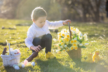 Beautiful stylish toddler child, boy, playing with Easter decoration in the park