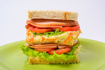Big sandwich with smoked ham, with lettuce and tomato on green plate. Fast food.