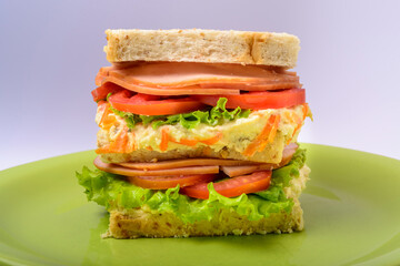 Big sandwich with smoked ham, with lettuce and tomato on green plate. Fast food.
