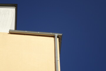 Upper right corner of yellow and white house wall with rain gutter, clear blue sky, use: copy...