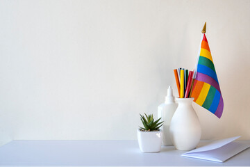 LGBT office, desk with rainbow flag and stationery, blank wall with space for text