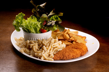 meal plate with spatzle, potatoes, breaded chicken breast and lettuce salad with cherry tomatoes on wooden table