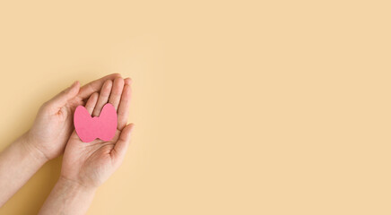 World Thyroid Day. Women's hands hold a paper form of the thyroid gland on beige background. Problems with thyroid. Polycystic disease. World cancer day. copy space. banner