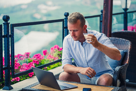 male businessman working on laptop at rooftop cafe with beautiful panoramic view. Guy blogger drinks coffee and works on a computer while traveling