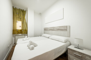 Bedroom with king size bed with long pillows on the headboard, bedside table with lamp, aluminum radiator and window with silk curtain