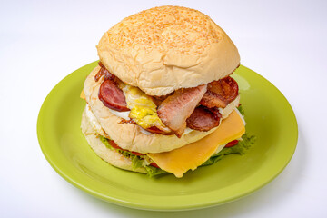 Big hamburger sandwich with smoked ham, cheese, eggs, sausage, bacon, lettuce and tomato on a green plate. Fast food.