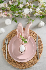 Easter dinner with white bunny, fresh spring flowers and eggs. Elegance pastel and pink tablescapes. View from above. Christian religion tradition. Vertical.