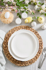 Easter table setting with yellow chick, organic eggs, fresh flowers on linen tablecloth. Vertical format.