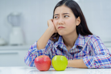 asian woman unhappy holding green apple and red apple.