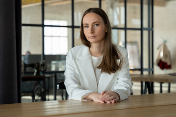 Obraz premium Pretty happily smiling woman looking into the camera is sitting at a desk in the office. 