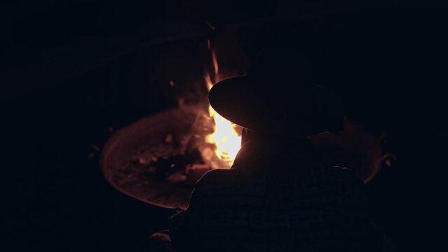 Silhouette of lonely cowboy sitting by bonfire on dark night, back view