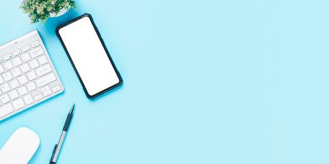 Office desk with computer keyboard, Blank screen smart phone, mouse, pen on blue background, Top view with copy space, Mock up..