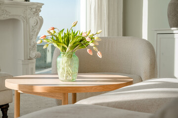 A bouquet of tulips in a beautiful vase at home in a bright modern interior on a wooden table. Spring concept