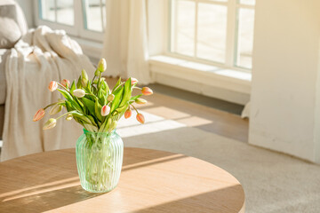 A bouquet of tulips in a beautiful vase at home in a bright modern interior on a wooden table....