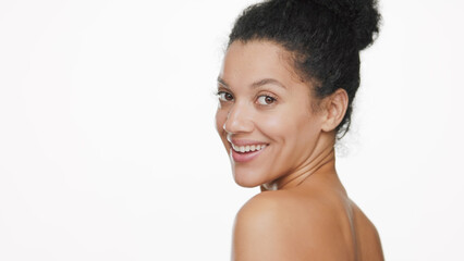 Beauty portrait of young African American woman with curly hair in bun looks at the camera over her shoulder on white background | Beauty care commercial concept