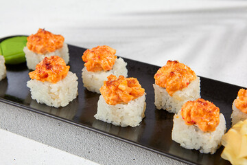 Maki sushi with salmon top on black plate. Sushi roll with philadelphia cheese inside and salmon tartare outside. Maki roll in minimal concept. Summer menu for japanese restaurant.