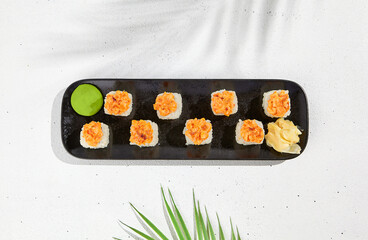 Maki sushi with salmon top on black plate. Sushi roll with philadelphia cheese inside and salmon tartare outside. Maki roll in minimal concept. Summer menu for japanese restaurant.