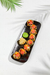 Tempura sushi roll with grapefruit and mango sauce. Hot maki sushi in black plate on white background. Summer menu for japanese restaurant. Modern sushi menu with hard shadow and leaves.