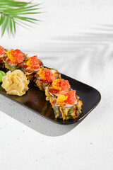 Tempura sushi roll with grapefruit and mango sauce. Hot maki sushi in black plate on white background. Summer menu for japanese restaurant. Modern sushi menu with hard shadow and leaves.