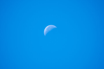 White moon crescent seen in the blue daytime sky