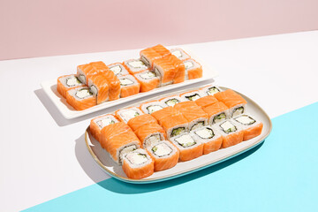 Set of salmon sushi rolls. Philadelphia maki in ceramic dishware on coloured backdrop. Sushi menu concept. Modern japanesse food. Maki sushi with salmon in minimal style