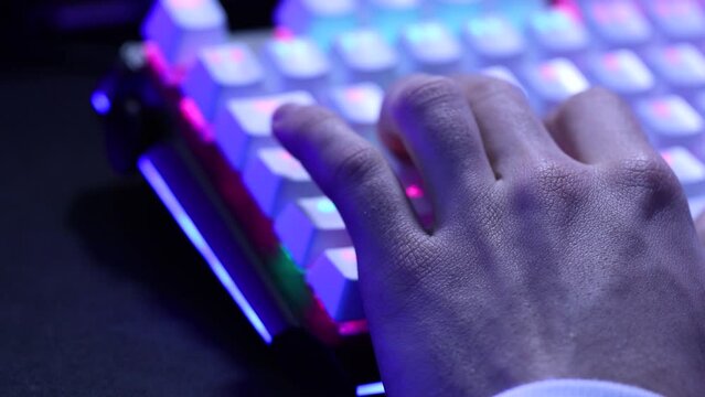 Young man hand using the W, A, S, D keys of a mechanical keyboard with led lights. Blue and purple illuminated gamer keyboard macro shot in 4k.
