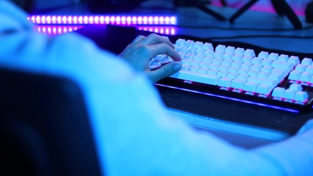 Young man hands using the W, A, S, D keys of mechanical keyboard with led lights. Blue and purple illuminated gamer keyboard macro shot in 4k.