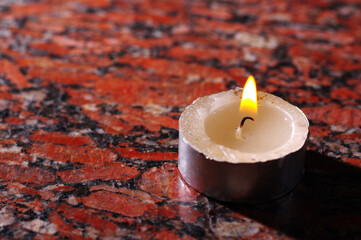 A burning candle and a glass beaker on a granite slab. 