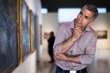 Adult man is visiting museum and looking at the pictures in the gallery indoor.