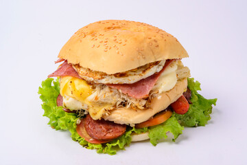 Big hamburger sandwich with smoked ham, cheese, eggs, sausage, bacon, lettuce and tomato on white background.