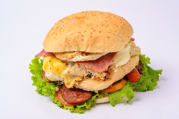 Big hamburger sandwich with smoked ham, cheese, eggs, sausage, bacon, lettuce and tomato on white background.